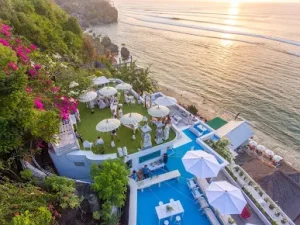 Elegant cliffside venue in Uluwatu overlooking the ocean at sunset, with stylish white decor and guests enjoying a scenic gathering a luxurious escape included in the Best Things to Do in Uluwatu, perfect after a serene Bingin silver class session.