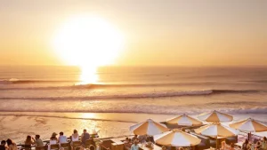 Golden sunset over the ocean viewed from a beachfront restaurant in Uluwatu, where guests relax under umbrellas with waves rolling in a must-see moment listed among the Best Things to Do in Uluwatu, ideally after a soothing Bingin silver class session.